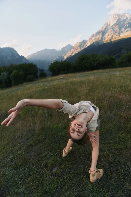 Young girl balances in a playful backbend on a grassy mountainside, enjoying the outdoors and fresh mountain air.