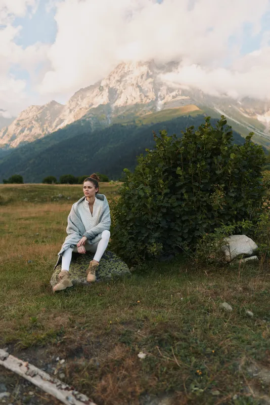 Young woman in casual clothes sitting on a bench near a bush with mountain landscape in the background. Outdoor lifestyle, nature, and relaxation concept.