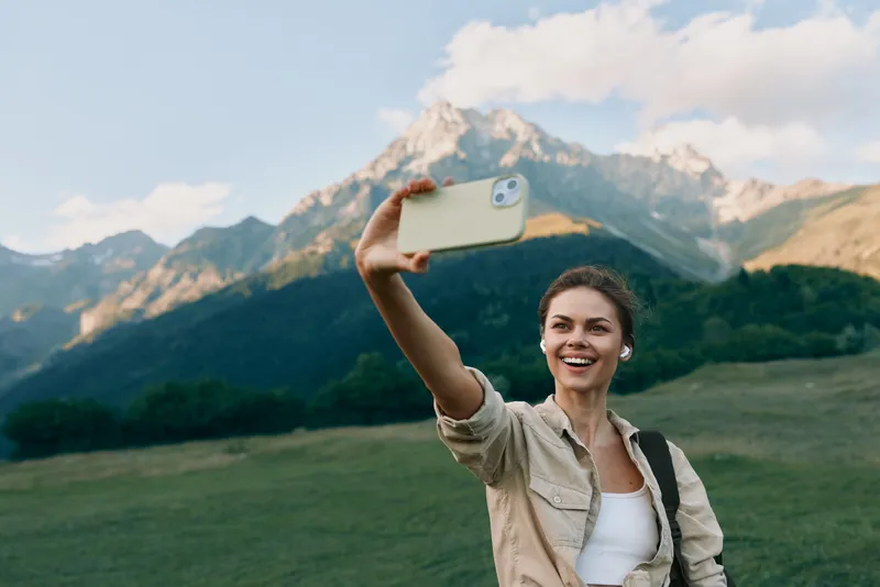 A cheerful woman takes a selfie in a scenic mountain meadow, casual jacket, sunny day. Lifestyle portrait capturing outdoor exploration and joyful travel moments, authentic, bright, modern.