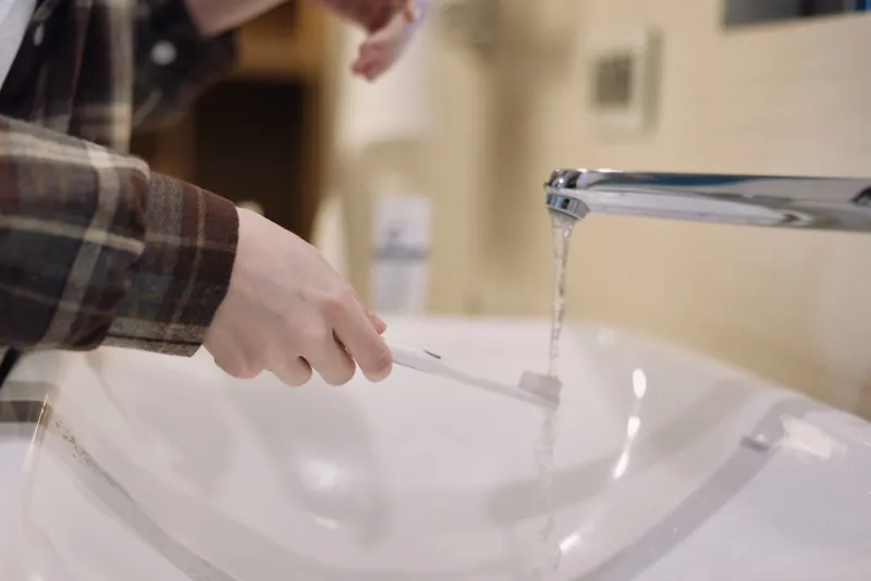 Closeup of a person brushing teeth at a bathroom sink with running water from a faucet, illustrating daily dental hygiene and routine care in a modern home.
