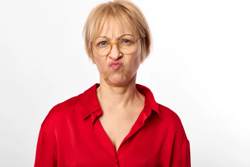 Elderly woman, glasses, red blouse, portrait, face, looking at camera, studio close up, serious expression, white background