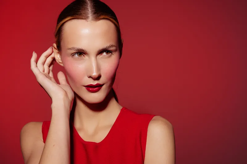 Portrait of a woman with slicked back hair wearing red dress and dark red lipstick on red background. Concept of fashion, beauty, elegance, and confident style.