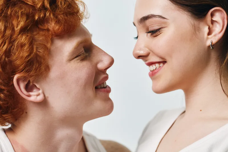 Couple, young man and woman looking at each other with smile and close face, love and relationship, intimacy and happy moment on light background. Portrait, together and connection.