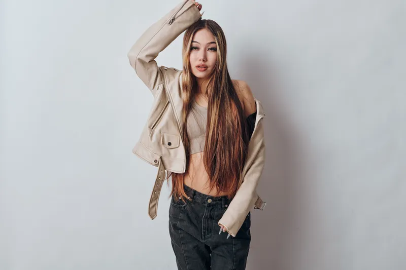 Young woman with long hair wearing trendy casual jacket and top posing against white background. Fashion, style, beauty, confident female model with streetwear and natural look in studio.