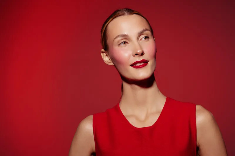 Portrait of a confident woman with red lipstick and red dress against a red background. The image highlights beauty, fashion, and elegance with a bold color theme.