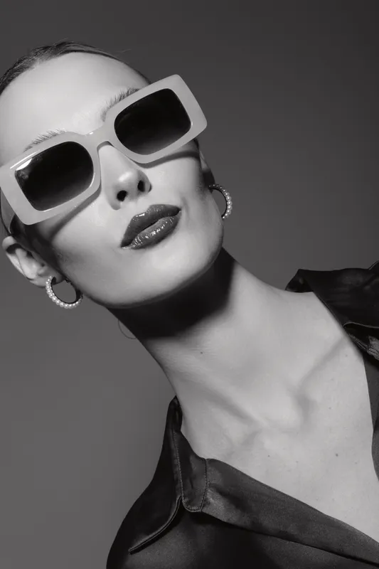 Elegant white woman with pale skin wearing large sunglasses and hoop earrings, posing with confident expression in studio.