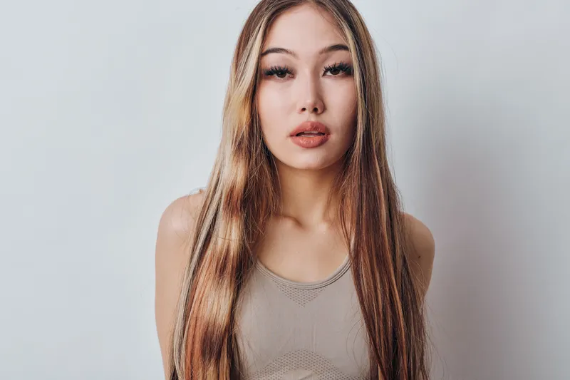 Woman with long hair and natural makeup posing on light background for beauty, fashion, portrait, and hairstyle concept with casual clothes and serious expression in studio.