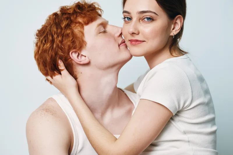 Couple, love, intimacy and affection with young man and woman embracing and kissing on light background. Emotional, romantic, relationship and close connection between people in studio.