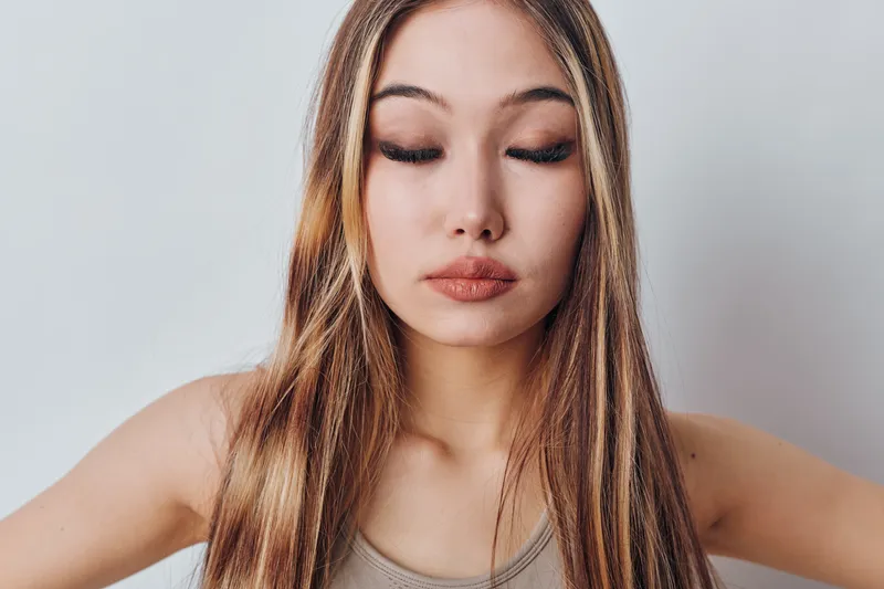 Young woman with long hair and closed eyes posing in casual top on light background. Beauty, calm emotion, and portrait with natural makeup and smooth skin in studio.