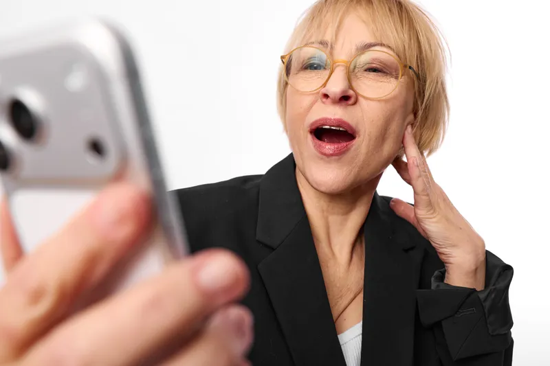 Woman smartphone glasses talking surprised communication portrait technology, studio light, hand at ear, closeup selfie gesture, indoor background, digital call