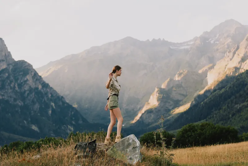 Young woman in casual outfit walks on rock in mountain valley during daytime, enjoys nature and outdoor lifestyle with scenic landscape background.