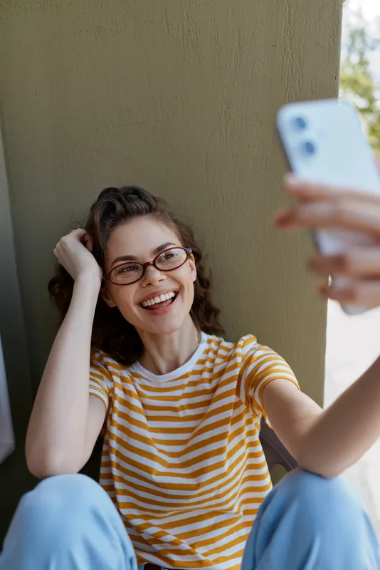 Smiling woman wearing a striped shirt taking a selfie at home, casual lifestyle moment, relaxed expression, bright natural light, cozy interior, everyday joy, self expression, candid portrait.