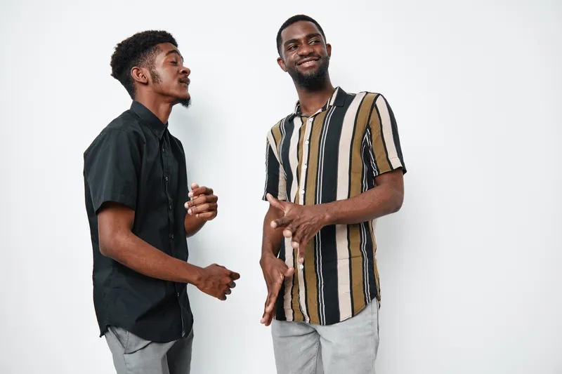 Two young black men with dark skin standing and talking together in casual clothes against white background. African ethnicity, friendship and communication concept.