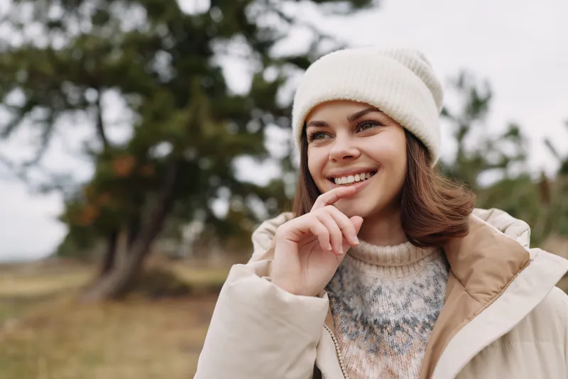 Woman outdoors smiling winter coat beanie, wearing a cozy look on a cool day, a natural portrait with a blurred park backdrop and soft light.