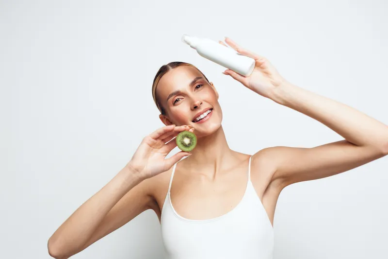 Woman applying cucumber on face, smiling, studio skincare and self care wellness, light cream on cheek, close up portrait on white background, beauty spa routine, healthy glow concept