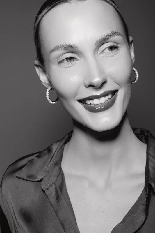 Portrait of a smiling Caucasian woman with fair skin and slicked-back hair wearing hoop earrings and a silky blouse. Concept of beauty, fashion, and elegance in studio lighting.
