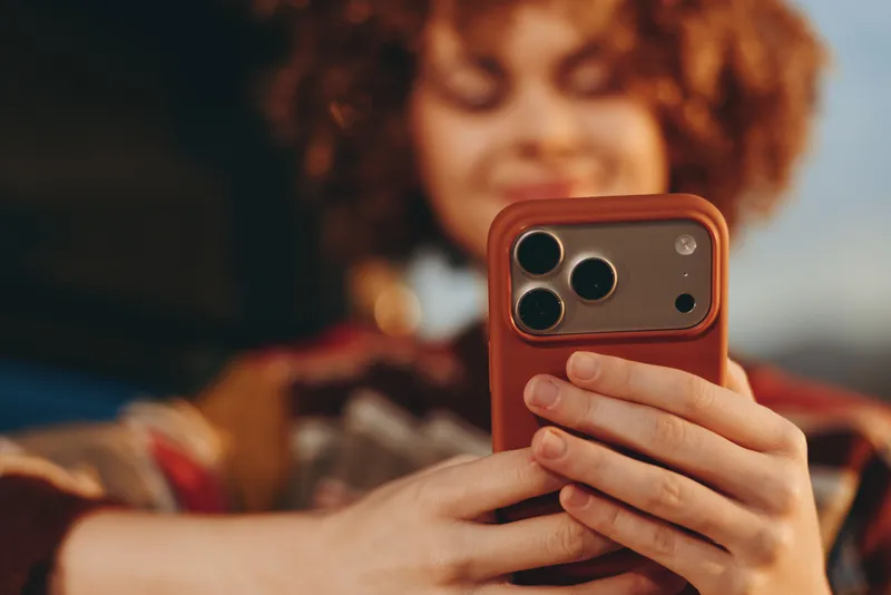 Woman lifestyle selfie with smartphone, curly hair and hands holding phone, blurred warm background bokeh, candid closeup portrait, modern communication moment