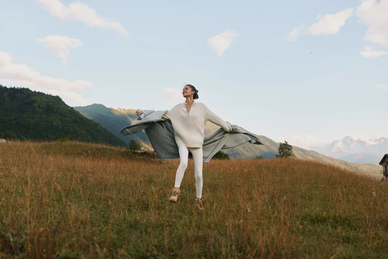 A young woman in white casuals twirls in a sunlit meadow, her flowing fabric catching the breeze as she enjoys open space and a feeling of freedom.