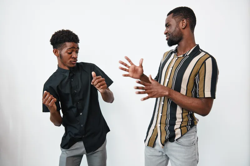 Two African American men with dark skin dancing and enjoying music together in casual clothes against white background. Friends having fun and expressing joy indoors.
