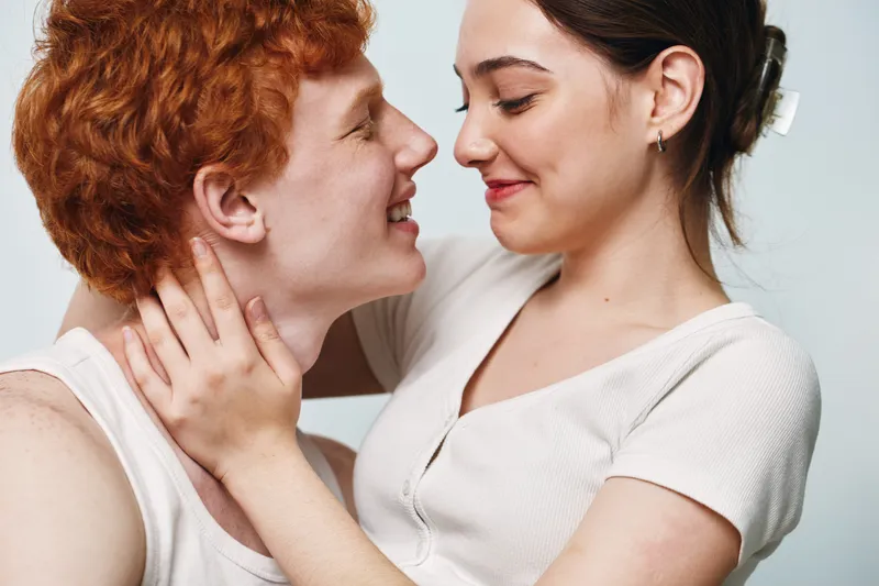 Couple, love, young, smiling and close face to face with hands on neck. Woman and man in casual clothes looking at each other with happiness and tenderness on neutral background.