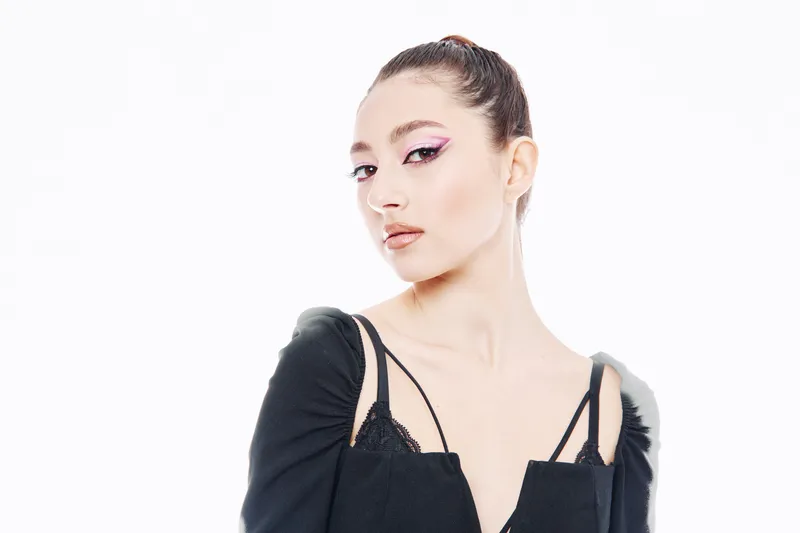 Young stylish woman in creative fashion outfit posing against a white background. Focus on unique makeup and confident expression in a beauty and creative style concept.