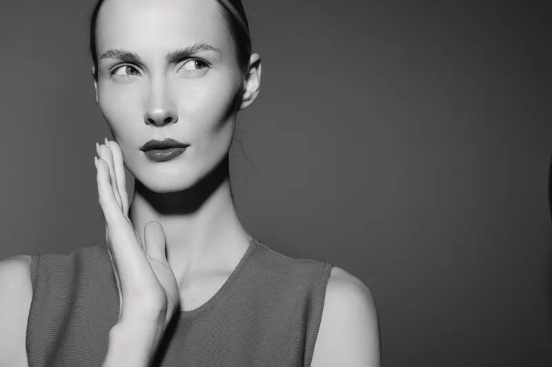 Portrait of a fair skinned white woman with short hair looking away, hand near face. Black and white studio image highlighting elegance and thoughtful expression in fashion concept.