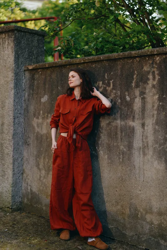A woman in a red jumpsuit leans against a weathered wall outdoors, showcasing a casual, stylish street pose. Concept: contemporary fashion, confidence, and relaxed lifestyle