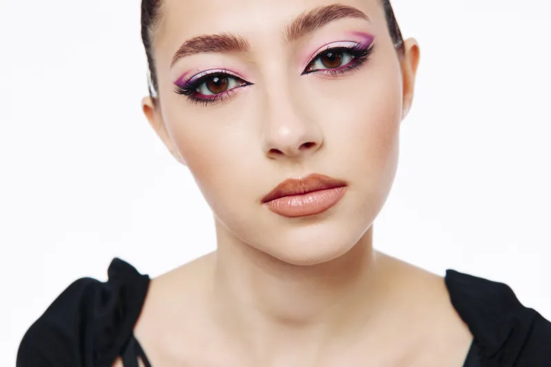 Close-up portrait of young woman with creative violet eyeshadow and glossy nude lipstick. Stylish fashion makeup on flawless skin, treted in bright studio light on white background.