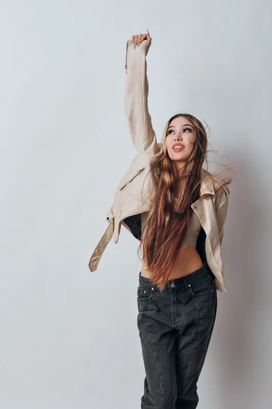 Young woman with long hair posing in casual jacket and black jeans on grey background. Fashion model expressing dynamic movement and street style with confident expression.