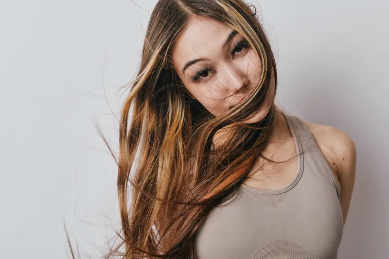 Young woman with long hair playing with strands in front of face wearing casual tank top on white background for beauty and lifestyle concept.