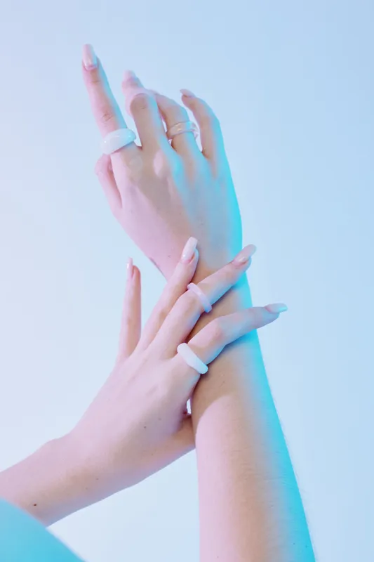 Close-up of a woman beauty fashion hands with long nails and white rings. The hands are crossed with soft blue lighting on a light background. Concept of elegance and style.