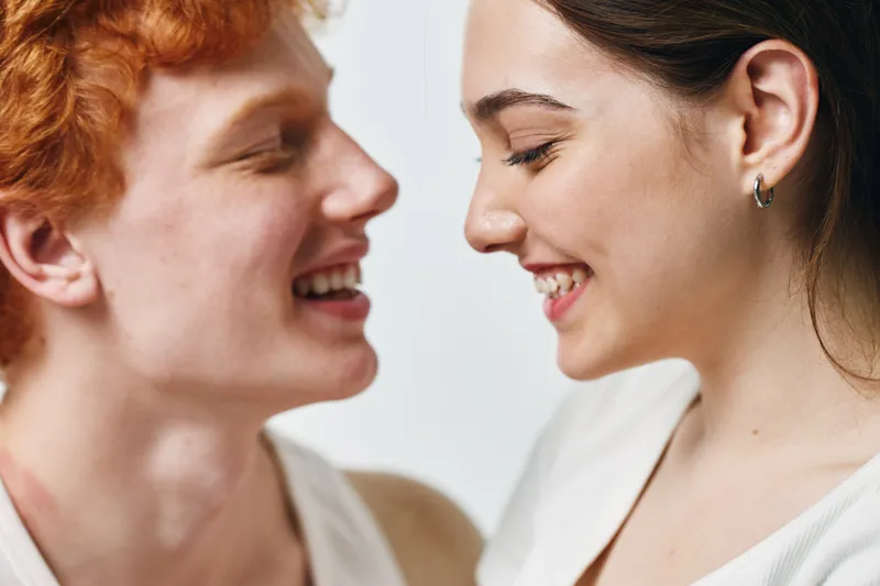 Young man and woman smiling closely with eyes closed in intimate moment, showing affection and happiness on light background. Positive emotion and connection between couple.
