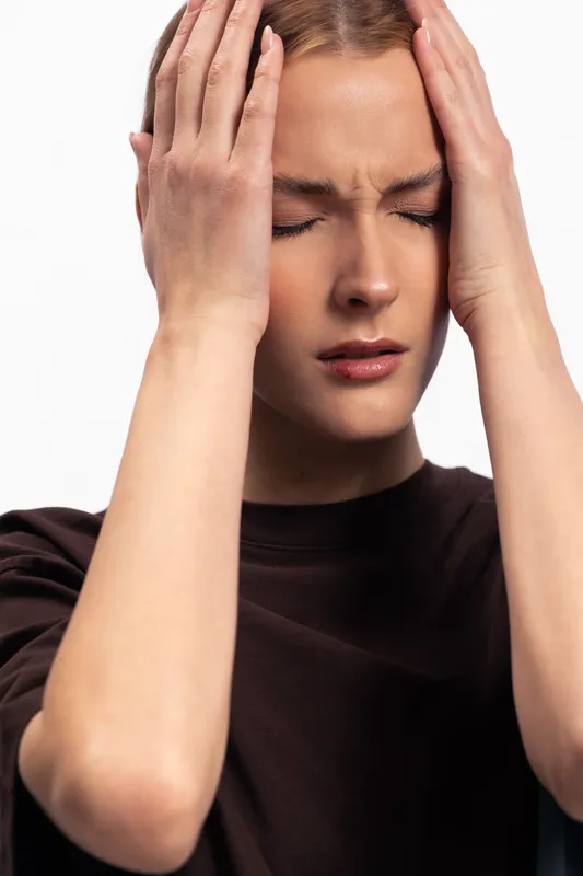 Young woman with closed eyes holds head with both hands, expressing stress and headache. Isolated on white background. Concept of pain, tension, and emotional discomfort.