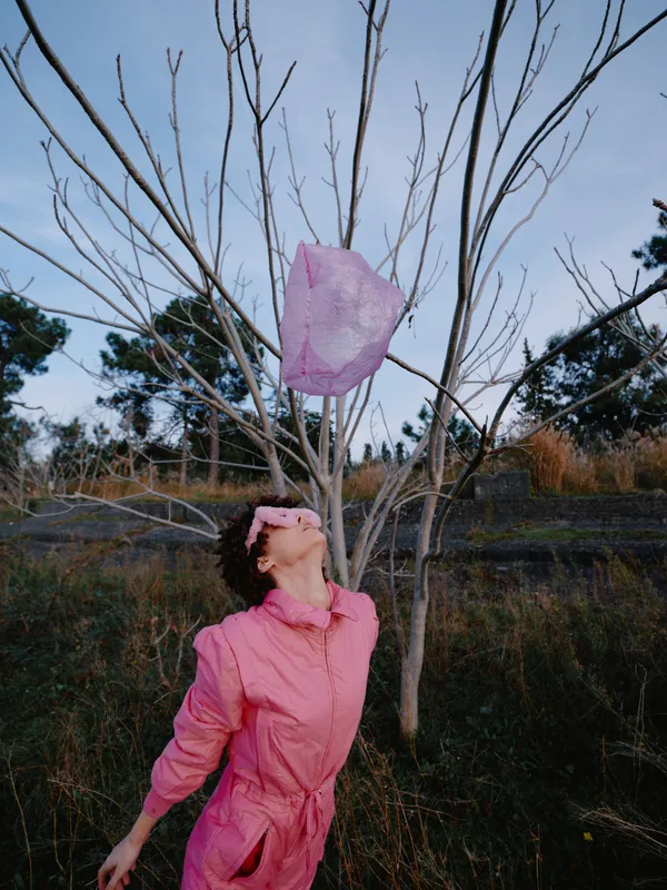 Lantern release outdoors with a woman in a pink jumpsuit beneath leafless trees, bright sky, capturing joy, freedom, and a intimate connection with nature