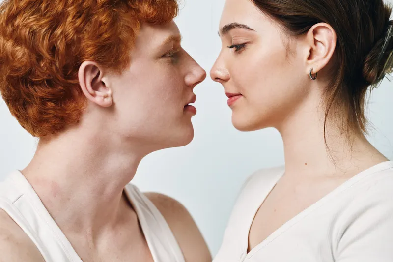 Couple with red hair and brunette facing each other closeup for intimacy and relationship love. Young man and woman touching noses with eyes closed for affection and connection in studio.