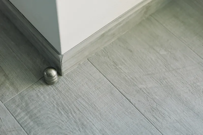 Close up of a modern interior corner featuring a cabinet leg and a small metal ball resting on light wood floor, highlighting texture and soft shadows.