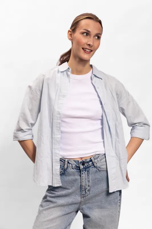 Young woman in casual outfit with light shirt and jeans poses confidently against white background. Concept of casual fashion, youth, and relaxed style for lifestyle and modeling.