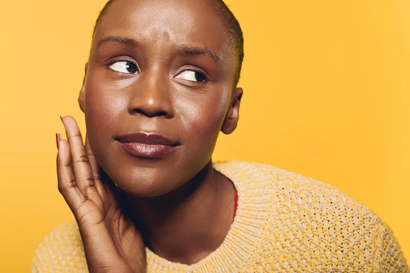 Close-up of a thoughtful dark skinned African woman with short hair wearing a yellow knit sweater on yellow background. Concept for contemplation, emotion, and natural beauty.