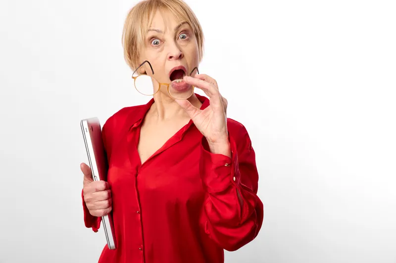 Shocked surprised woman in red blouse holds a smartphone, mouth open and wide eyes, gripping the device close. Clean white background, portrait concept of sudden news.
