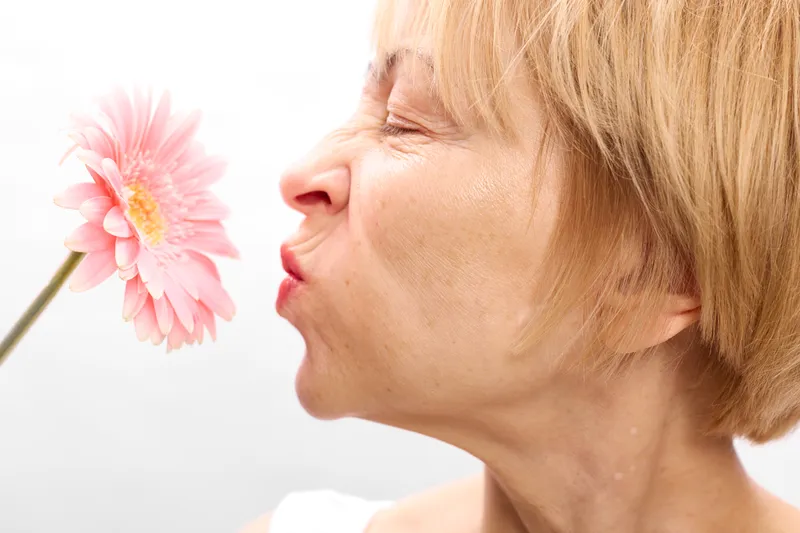 Woman closeup face profile smelling pink flower blossom, blonde hair, calm spring nature, soft light, white background, serene expression, gentle tenderness