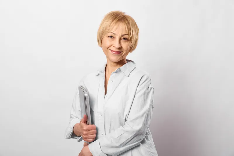 Smiling doctor in white coat holds smartphone, healthcare technology for telemedicine communication, calm professional pose in bright background, remote care assistance
