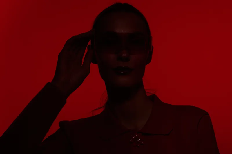 Silhouette of a woman wearing sunglasses against a red background. The moody lighting creates a mysterious and stylish concept of fashion and portrait photography.
