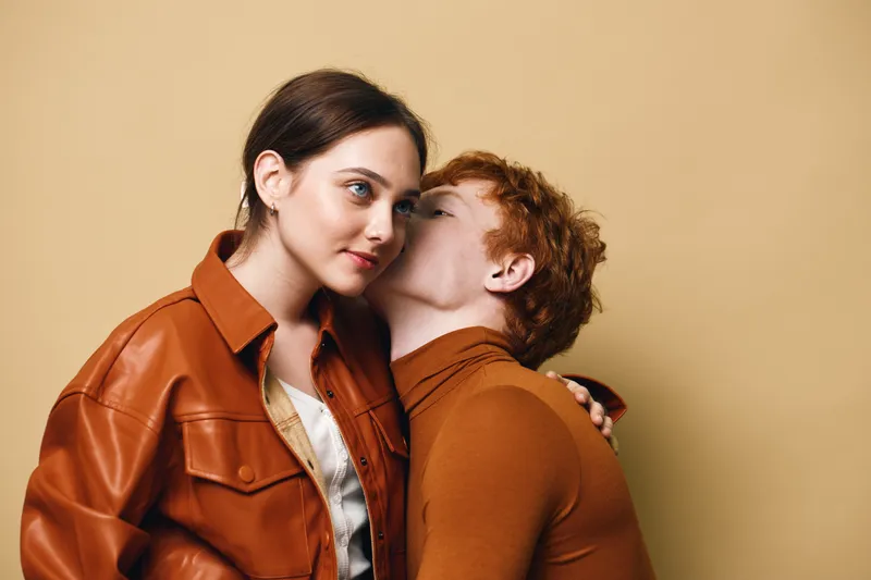 Couple, young man and woman in autumn clothing with affectionate gesture and intimacy on beige background. Relationship, love and connection with casual style and warm colors.