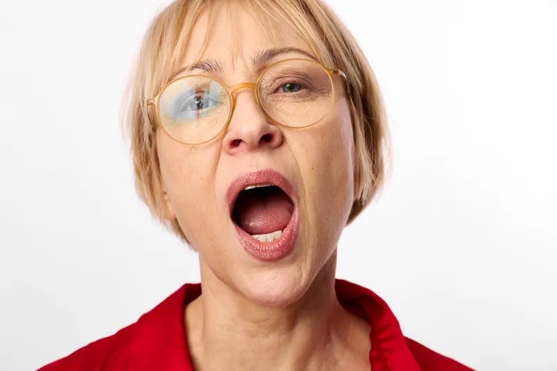 Blonde woman surprise, shocked expression with round glasses, open mouth, focused gaze, red hoodie, closeup portrait, isolated white background, emotion