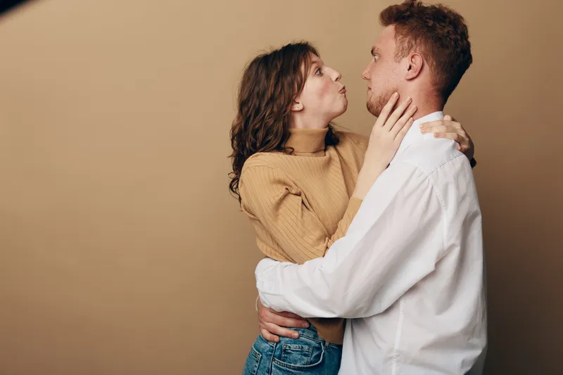 Young couple embraces and looks at each other with affection on beige background. Casual clothing and warm mood create concept of love, relationship, and intimacy.