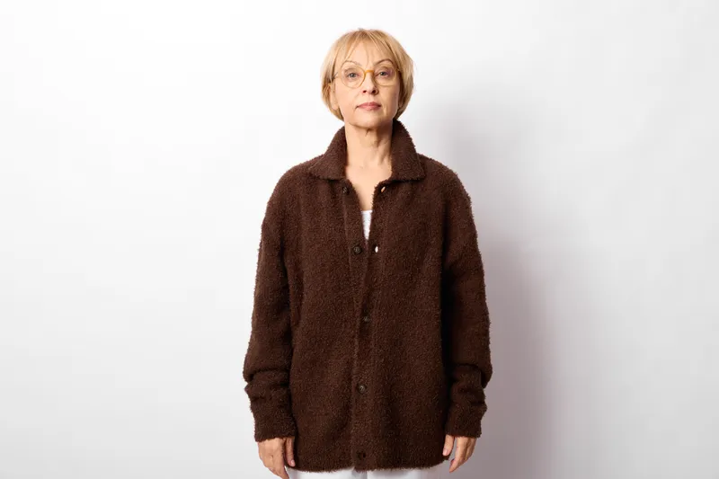 Woman portrait with glasses, standing in studio, wearing a brown coat, against a white background, calm mood, soft studio lighting, fashion style, neutral face