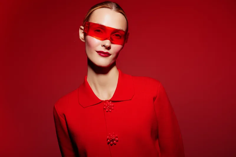 Portrait of a confident woman wearing red sunglasses and a red textured jacket against a red background. Concept of fashion, style, and bold color contrast in studio lighting.
