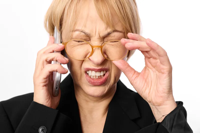 Businesswoman with glasses is laughing into phone in an office, professional suit, close up portrait, communication concept, mood, modern corporate background, soft daylight.