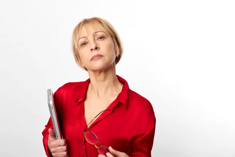 Senior woman in red blouse holds an open book, looking thoughtful at camera, studio portrait on white background, calm mood, education and reading concept, copy space