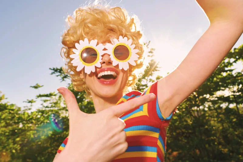 Cheerful child outdoors wearing sunflower sunglasses, playful pose in a sunlit garden, retro film color vibe, bright natural tones, carefree mood, vivid moment